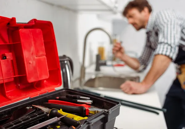 Plumber fitting a tap, toolbox in the foreground